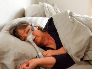 Middle Aged Woman With Sleep Apnea Asleep in a Bed Wearing a CPAP